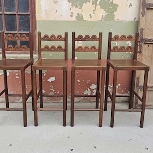 May include: A set of four tall wooden bar stools with square seats and straight legs. Each stool features a backrest composed of two horizontal slats, with each slat decorated with a series of carved, repeating semi-circular arch patterns.