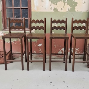 May include: A set of four tall wooden bar stools with a dark brown finish. Each stool features a square seat, four straight legs with connecting footrests, and a backrest designed with a distinct horizontal wavy or scalloped wooden slat.