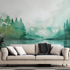May include: A wall mural featuring a watercolor landscape of green pine trees reflected in a calm lake. The scene is set behind a beige sofa with light-colored cushions and a dark gray throw blanket, placed on a black and white patterned rug.