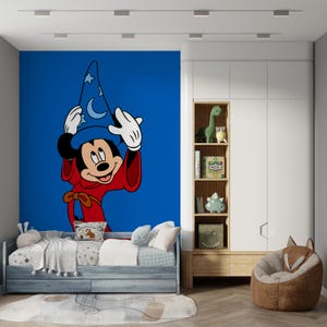 May include: A wall mural featuring Mickey Mouse as a sorcerer wearing a blue hat with moon and star patterns and a red robe, set against a solid blue background. The mural is positioned behind a bed with white bedding and a wooden storage unit.