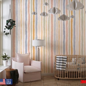 May include: A nursery room with a pastel striped wallpaper in shades of blue, yellow, pink, and green. The room features a pink armchair, a wooden crib, and paper cloud decorations. A lamp and hanging plant add to the decor.