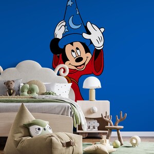 May include: A large wall decal featuring Mickey Mouse as a sorcerer, wearing a blue hat with stars and moons and a red robe, positioned against a solid blue wall. The character has white gloves and is shown from the waist up in a cartoon style.