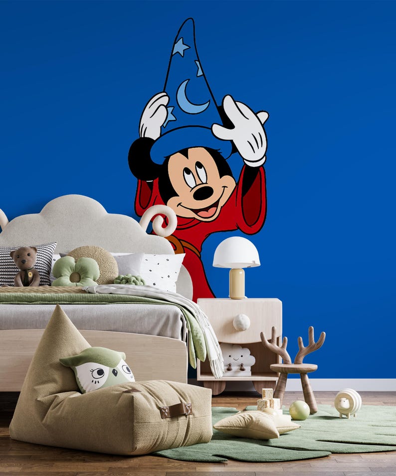 May include: A large wall decal featuring Mickey Mouse as a sorcerer, wearing a blue hat with stars and moons and a red robe, positioned against a solid blue wall. The character has white gloves and is shown from the waist up in a cartoon style.