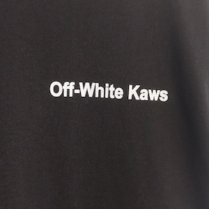 May include: Dark charcoal gray sweatshirt with the text "Off-White Kaws" in white block letters. The sweatshirt is made of a soft material and has a crew neck. The image is a close-up of the front of the shirt.