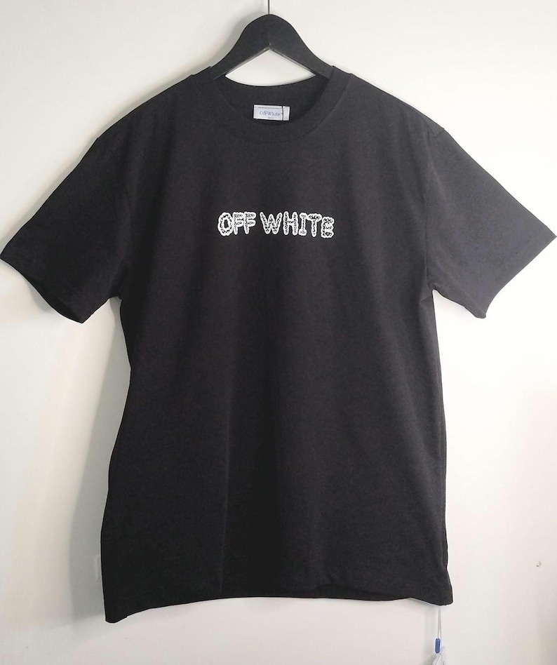 May include: Black t-shirt with the text "OFF WHITE" in white, displayed on a black hanger. The shirt has short sleeves and a crew neck. The text appears to be a brand name.