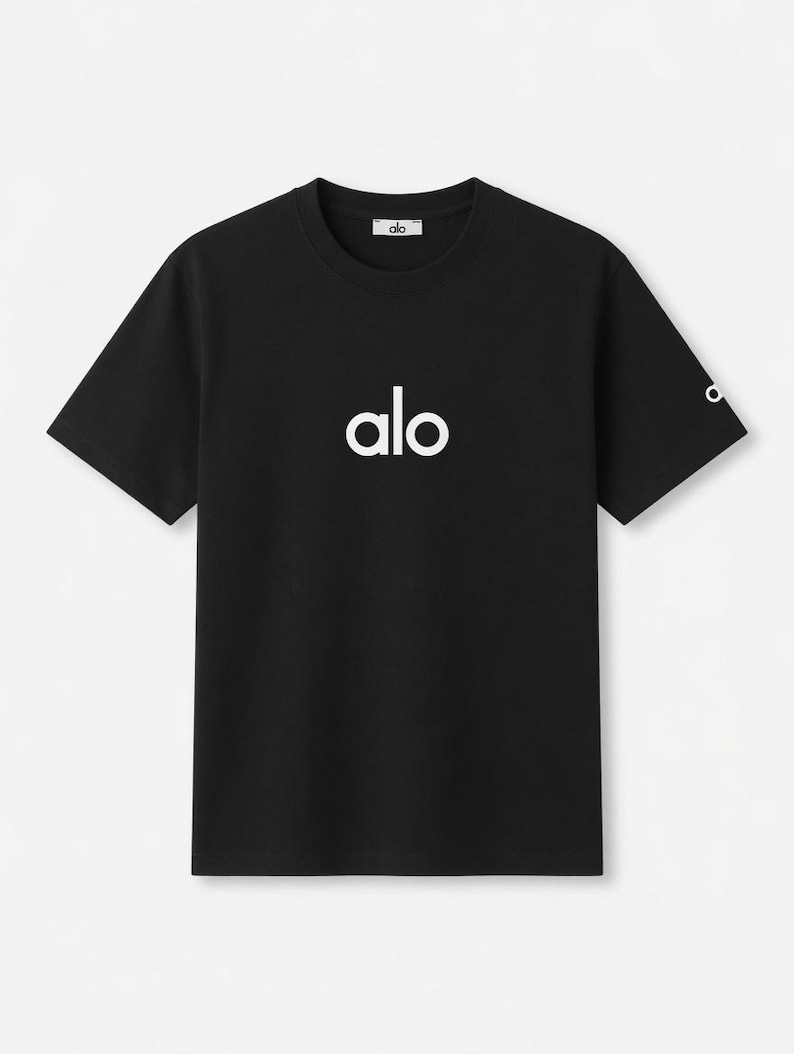 Op de afbeelding: Zwart T-shirt met ronde hals en het witte woord "alo" op de borst gedrukt. De merknaam "alo" staat ook in het wit op de bovenrug en op de linkermouw. Het T-shirt heeft korte mouwen.