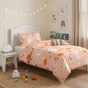May include: A twin bed featuring a light peach-colored comforter and pillowcase decorated with a repeating pattern of white ghosts, orange pumpkins, black spiders, and the word BOO. Three plush toys sit on the bed, and a ghost-shaped lamp sits nearby.