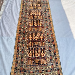 May include: A rectangular, patterned rug with a central design of repeating geometric shapes in red, gold, and navy blue. The rug has a border of gold and a fringe at the ends. The rug is likely used as a runner.