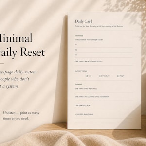 Pode incluir: Um cartão de reinicialização diária minimalista com o texto "Minimal Daily Reset" e "Daily Card". O cartão inclui prompts para a manhã, a noite e os níveis de energia. Uma chávena e um vaso de cerâmica bege com flores secas estão à direita.