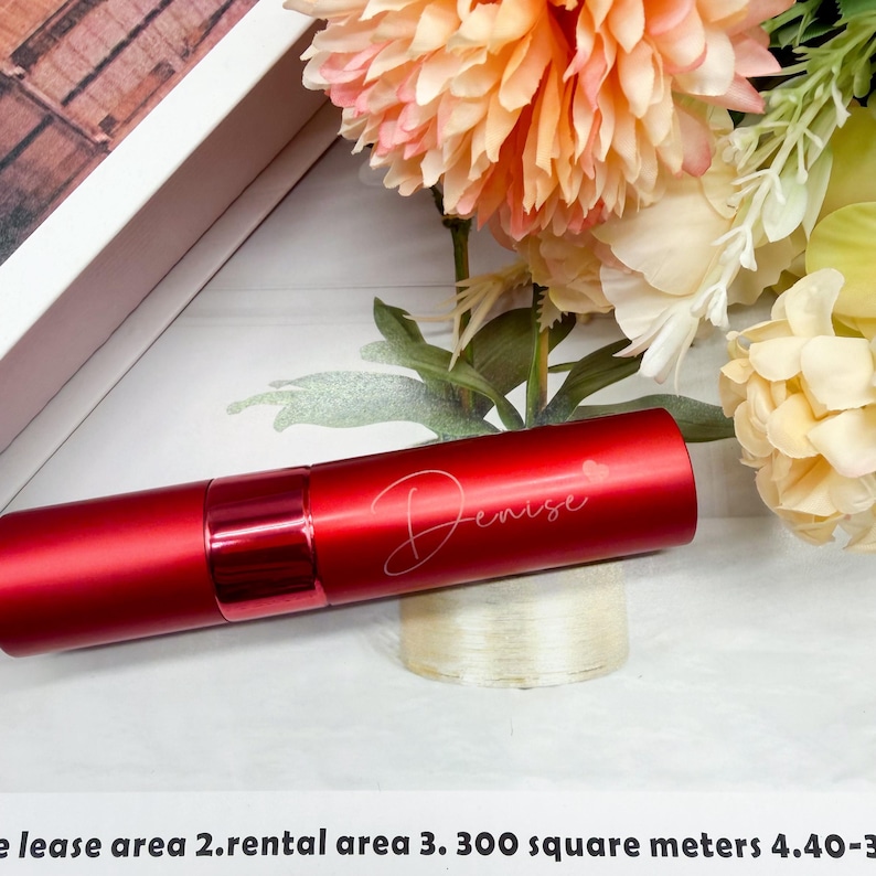 May include: A cylindrical red metal perfume atomizer with a shiny finish and a matching red cap. The name Denise is engraved in a cursive script on the side of the bottle, accompanied by a small heart symbol above the letter i.