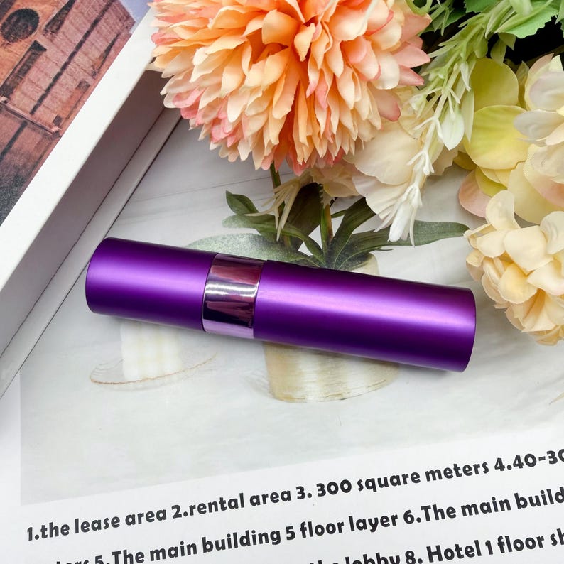 May include: A cylindrical purple atomizer bottle with a matte finish and a glossy metallic purple band around the center. The container is a solid, opaque purple color and features a smooth, uniform surface design for holding liquid contents.