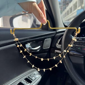 May include: A gold-toned metal car visor hook featuring a double-layered chain attachment. The two delicate gold chains are adorned with small, irregular, translucent yellow crystal chips spaced evenly along the length of the metal links.