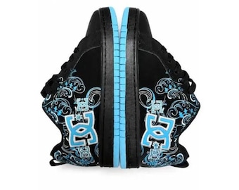 May include: A pair of black trainers featuring a light blue DC logo on the side, accented with intricate light blue and white swirling patterns. The shoes have black laces, black soles, and a light blue trim along the edge of the sole.