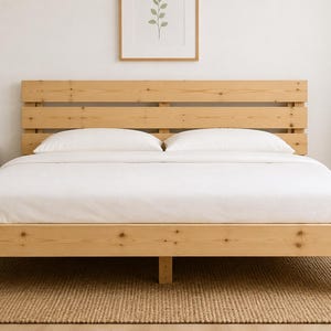 May include: A light-colored wooden bed frame featuring a horizontal slatted headboard and a low-profile base. The bed is dressed with white bedding, including two pillows, and is constructed from natural pine wood with visible grain and knots.