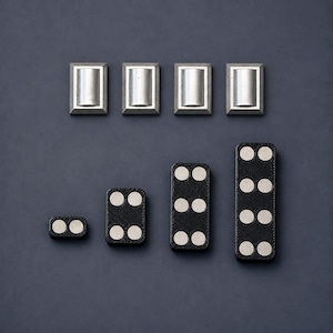 May include: Four rectangular silver-toned metal components with central cylindrical protrusions arranged in a row above four black rectangular pieces of varying lengths, each featuring circular silver-toned metal inlays in pairs.