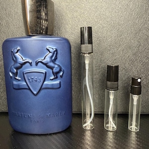 May include: A dark blue perfume bottle with a silver cap, embossed with two rearing horses and the text "1743". Three clear glass spray bottles with black caps are next to the perfume bottle.
