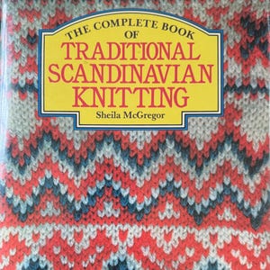 May include: A hardcover book titled The Complete Book of Traditional Scandinavian Knitting by Sheila McGregor. The cover features a vibrant, repeating knit pattern in shades of red, white, grey, and blue, with the title printed in red on a yellow background.