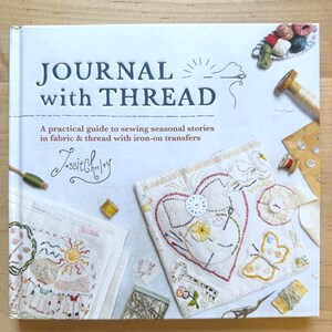 May include: A hardcover book titled Journal with Thread by Jessie Chorley. The white cover features embroidered fabric squares with heart, swan, and butterfly motifs, surrounded by scattered sewing supplies like thread spools and needles.