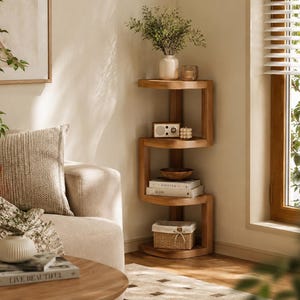 Puede incluir: Una estantería de esquina de madera de color marrón claro con un diseño en zigzag o en forma de S con cuatro niveles abiertos. Los estantes contienen un jarrón blanco con vegetación, una radio pequeña, un cuenco de madera y una cesta.