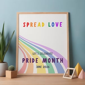 May include: A framed print with the words "SPREAD LOVE" in rainbow colors. Below, it reads "LET'S CELEBRATE PRIDE MONTH JUNE 2026" with a rainbow design. The frame is light wood, and the background is white.