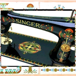 Könnte beinhalten: Eine schwarze Singer-Nähmaschine mit goldener Schrift und kunstvollen, farbenfrohen Blumen- und Geometriemustern. Der Maschinenkörper zeigt den Schriftzug The Singer Manufacturing Co und Singer, verziert mit stilisierten botanischen Motiven in Rot, Grün und Gold.