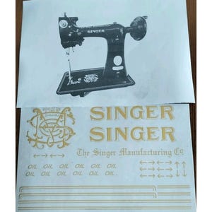 May include: A sheet of restoration decals for a Singer sewing machine, featuring a black and white illustration of the machine, gold Singer logos, the text The Singer Manufacturing Co, rows of the word OIL, and various gold line patterns.