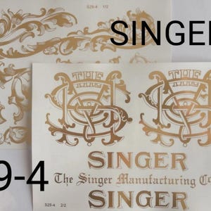 May include: Two sheets of gold-colored decals featuring ornate scrollwork and the text SINGER, THE, and The Singer Manufacturing Co. The designs include intricate flourishes and stylized lettering on a white background, labeled with 29-4 and S29-4.