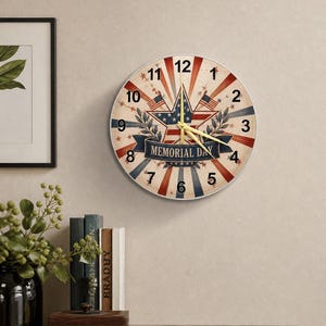 May include: A round wall clock with a patriotic design. The clock face features a star, American flags, and the text "MEMORIAL DAY" on a banner. The clock has red, white, and blue accents, with a white border and black numbers. The clock hands are yellow.