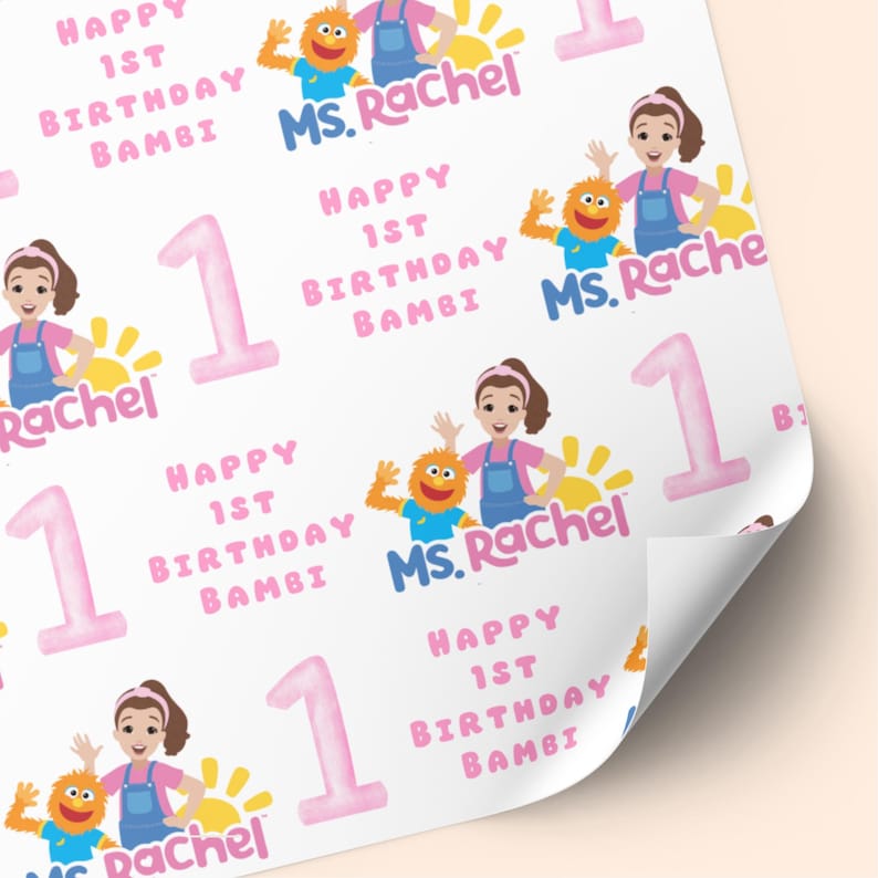 K&ouml;nnte beinhalten: Wei&szlig;es Geschenkpapier mit sich wiederholendem Muster. Das Design enth&auml;lt den Text "Happy 1st Birthday Bambi" und "Ms. Rachel" in Rosa und Blau. Illustrationen einer Frau, eines Monsters und der Zahl 1 sind ebenfalls vorhanden.