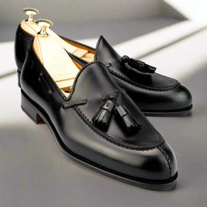 May include: A pair of black leather loafers with tassel details. The shoes have a polished finish, visible stitching, and a classic design. Shoe trees are inserted in the loafers. The loafers are a classic style.