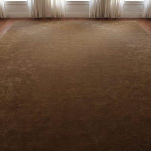 May include: A large, rectangular brown rug with a soft, plush texture. The rug fills the majority of the frame, with a dark brown hue. The rug is placed on a hardwood floor, with windows and white curtains in the background.
