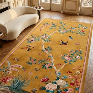 Könnte beinhalten: Ein rechteckiger Teppich mit senfgelbem Hintergrund und einem detaillierten botanischen Muster. Das Design zeigt einen zentralen blühenden Baum, verschiedene bunte Vögel im Flug sowie Gruppen blühender Pfingstrosen in Rosa, Weiß und Rot.