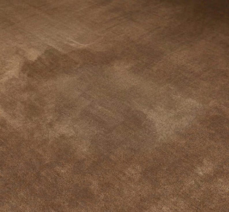 May include: A close-up shot of a brown, textured fabric. The fabric has a soft, velvety appearance with subtle variations in color and tone, creating a sense of depth and dimension. The surface appears to be smooth with a slight sheen.