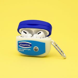 Könnte beinhalten: Eine weiß-blaue Hülle für kabellose Ohrhörer, die einem Vaseline-Erdölgelee-Behälter nachempfunden ist. Die Hülle hat einen blauen Deckel und einen silbernen Karabinerhaken. Die Ohrhörer sind weiß. Der Text "Vaseline pure petroleum jelly original" ist auf der Hülle aufgedruckt.