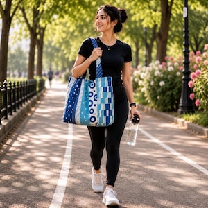 May include: A large tote bag featuring a patchwork design of various blue and white patterns, including stripes, circles, and squares. The bag has two shoulder straps and is constructed from fabric with a quilted texture in shades of navy and light blue.