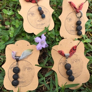 May include: Four necklaces with lava rock beads and fabric ribbon on display cards. The cards feature a moon-like design with a face.