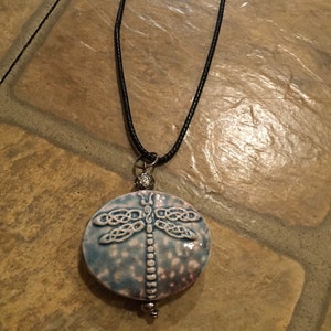 May include: A blue and white ceramic dragonfly pendant necklace with a black cord.