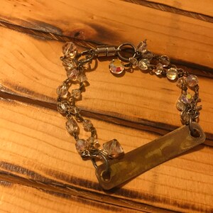 K&ouml;nnte beinhalten: Ein silbernes Armband mit einem rechteckigen Metallschild und Kristallperlen. Das Armband hat einen Magnetverschluss.