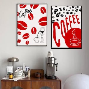 May include: Two framed coffee-themed art prints. One features red coffee beans and the word "Coffee" in script. The other has black coffee beans and the word "COFFEE" in bold red letters with a coffee cup illustration. Both are in black frames.