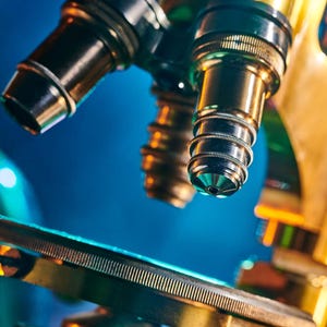 May include: Close-up of a vintage microscope with brass and black components. The lenses are in sharp focus, with a blurred background of laboratory equipment. The microscope is illuminated with blue and gold lighting.