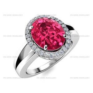 May include: A silver ring featuring a large, oval-cut, vibrant pink gemstone as the centerpiece. The stone is surrounded by a halo of small, clear, round-cut white stones set into the silver band. The text FM GEMS JEWELLERY appears repeatedly.