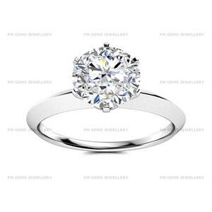 Può includere: Un anello color argento con una gemma trasparente, rotonda e sfaccettata, fissata da una montatura a sei griffe. La fascia è liscia e lucida, con il testo FM GEMS JEWELLERY ripetuto sullo sfondo dell'immagine in un carattere grigio chiaro.