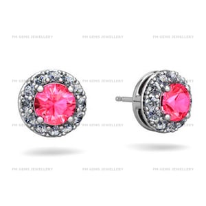 Puede incluir: Un par de pendientes de botón con una piedra central redonda de color rosa vibrante rodeada por un halo de pequeñas piedras blancas transparentes engastadas en metal plateado. El texto FM GEMS JEWELLERY se repite en el fondo.
