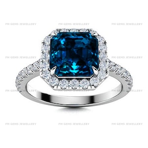 May include: A silver-toned ring featuring a large, rectangular, deep blue center stone surrounded by a halo of small, clear, round-cut stones. The band is also adorned with a row of small, clear stones. The text FM GEMS JEWELLERY appears repeatedly.