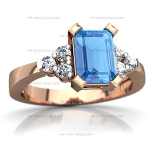 May include: A rose gold ring featuring a central emerald-cut blue gemstone held by four prongs, flanked by three small round white stones on each side. The text FM GEMS JEWELLERY is repeated across the image background.