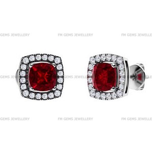 Può includere: Un paio di orecchini a lobo con una gemma rossa taglio cuscino, circondata da un alone di piccoli diamanti bianchi incastonati in metallo color argento. Il testo FM GEMS JEWELLERY è ripetuto sullo sfondo. Chiusura a perno con farfallina.