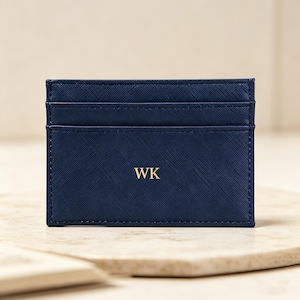 May include: A navy blue cardholder with three slots. The initials "WK" are printed in gold on the front. The cardholder is made of a textured material and is rectangular in shape.