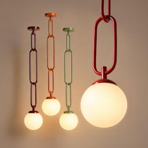 Op de afbeelding: Vier hanglampen met bolvormige witte glazen kappen, opgehangen aan lange, ovaalvormige metalen kettingen. De armaturen hebben glanzende afwerkingen in donkerrood, feloranje, saliegroen en een opvallende rode kleur op de voorgrond.