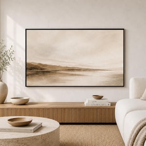 Könnte beinhalten: Ein großes, rechteckiges Wandbild in einem schwarzen Rahmen mit einer abstrakten Landschaftsdarstellung in Beige- und Brauntönen, die eine Horizontlinie über Wasser zeigt, platziert über einem hölzernen Medienmöbel in einem neutralen Raum.