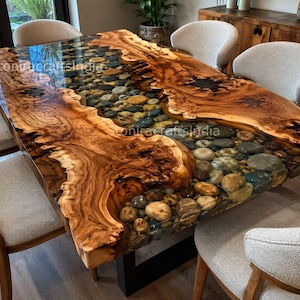 Peut inclure: Une table à manger rectangulaire composée d'une dalle de bois à bord naturel avec une section centrale en rivière remplie de galets lisses et multicolores incrustés dans de la résine transparente. Le texte "Stonicraftsindia" est visible.